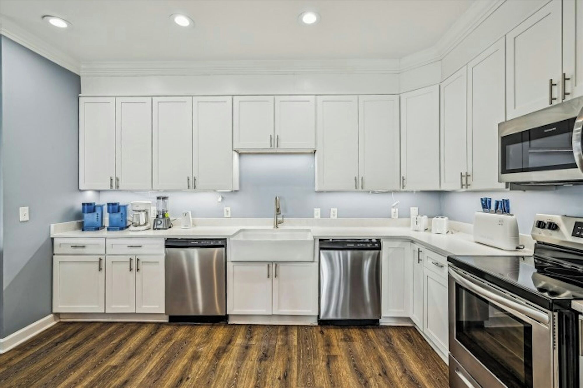 A modern kitchen with white cabinets, stainless steel appliances, and a wooden floor.