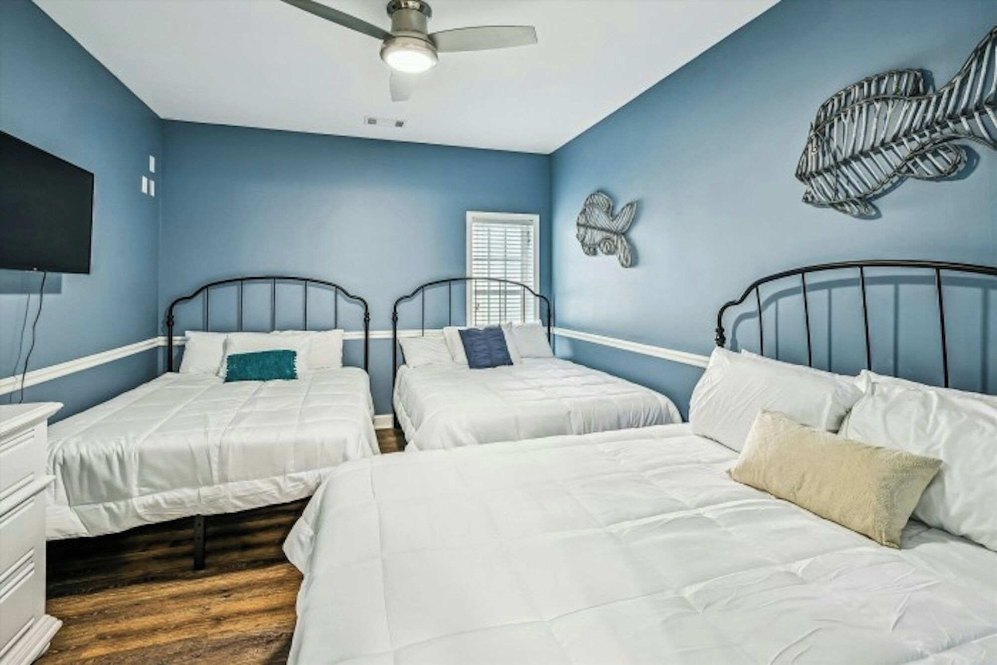 A bedroom with two single beds, a ceiling fan, a wall-mounted TV, and a window with blinds.