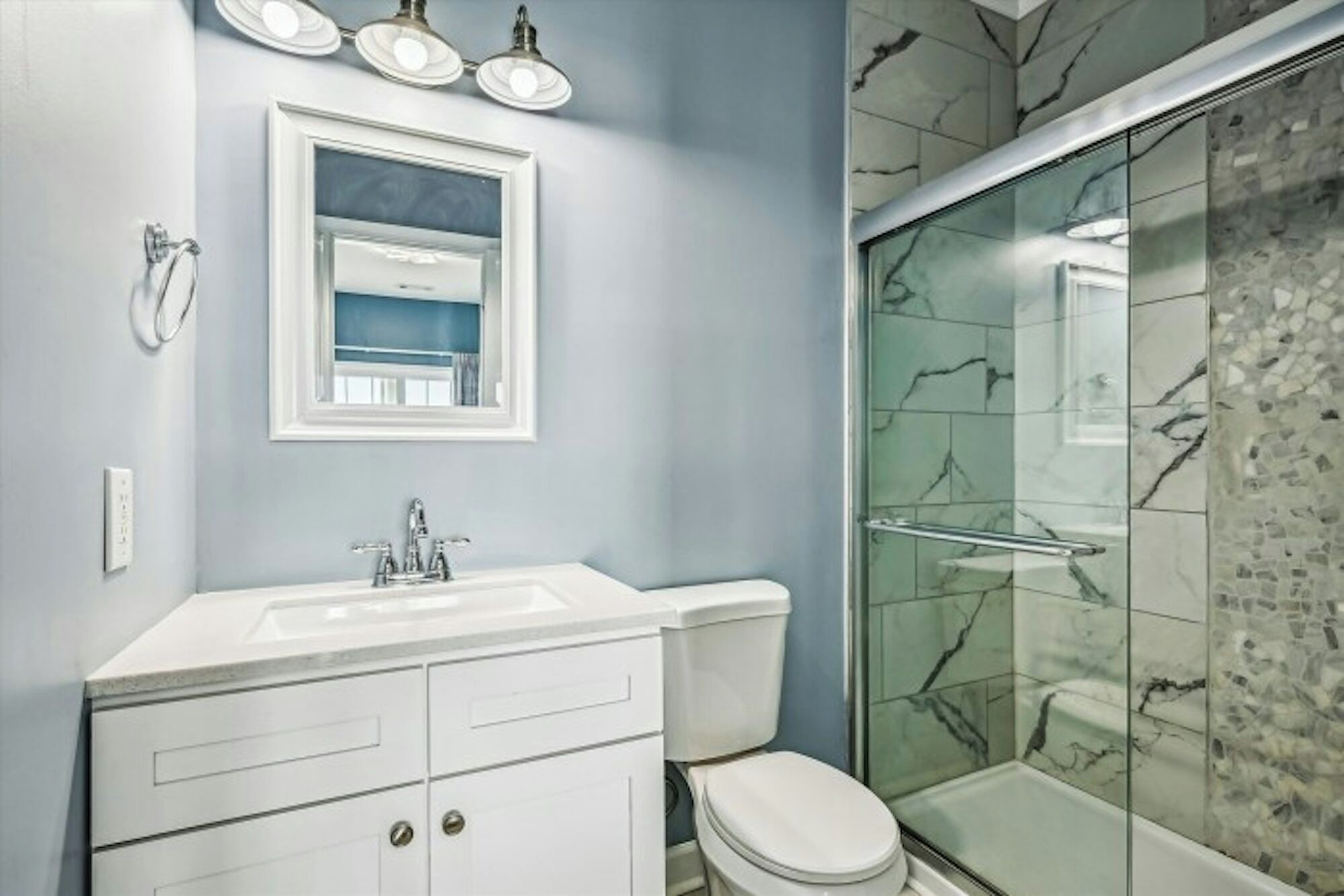 Une salle de bain avec un meuble-lavabo blanc, un miroir, des toilettes et une douche en verre avec des carreaux de marbre.