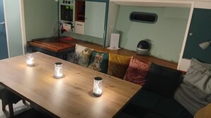 Un coin repas avec une table en bois, trois bougies allumées et un canapé agrémenté de différents coussins.