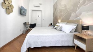 Une chambre avec un grand lit, une table de chevet avec une lampe, une chaise, un bureau et un téléviseur fixé au mur.
