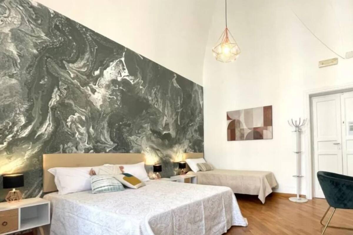 Quarto com um mural abstrato grande, duas camas, abajures, uma escrivaninha e uma cadeira.