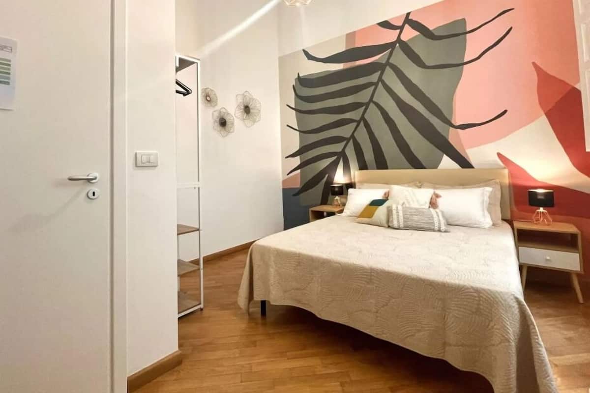 Quarto com cama, mesas de cabeceira e parede com padrão de folha.