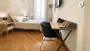 Une chambre à coucher comprenant un lit, une table de chevet, un bureau, une chaise et un téléviseur fixé au mur.