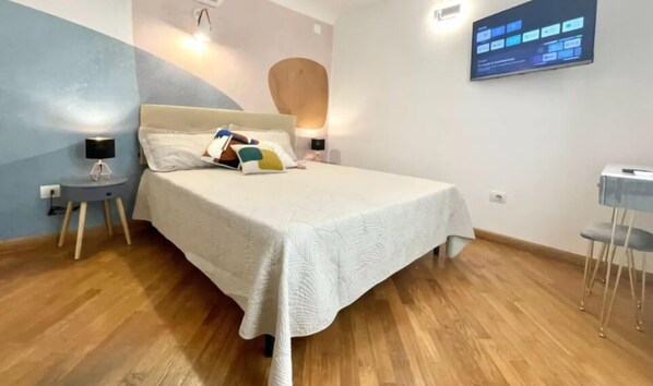 Un dormitorio moderno con una cama grande, lámparas de noche, una mesita pequeña y un televisor instalado en la pared.
