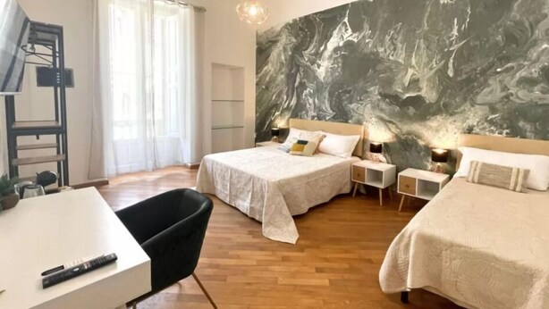 Une chambre d’hôtel avec deux lits, un bureau et une chaise. Un grand tableau abstrait orne le mur, et il y a une fenêtre avec des rideaux.