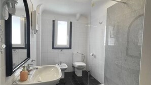Une salle de bain moderne avec un lavabo blanc, un bidet, des toilettes et une douche à parois de verre.