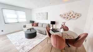 A modern living room with a sofa, coffee table, and dining area with chairs. - TownHome 3blks Boardwalk uB (Virginia Beach)