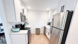 A modern kitchen with white cabinets, stainless steel appliances, and a wooden floor. - TownHome 3blks Boardwalk uB (Virginia Beach)