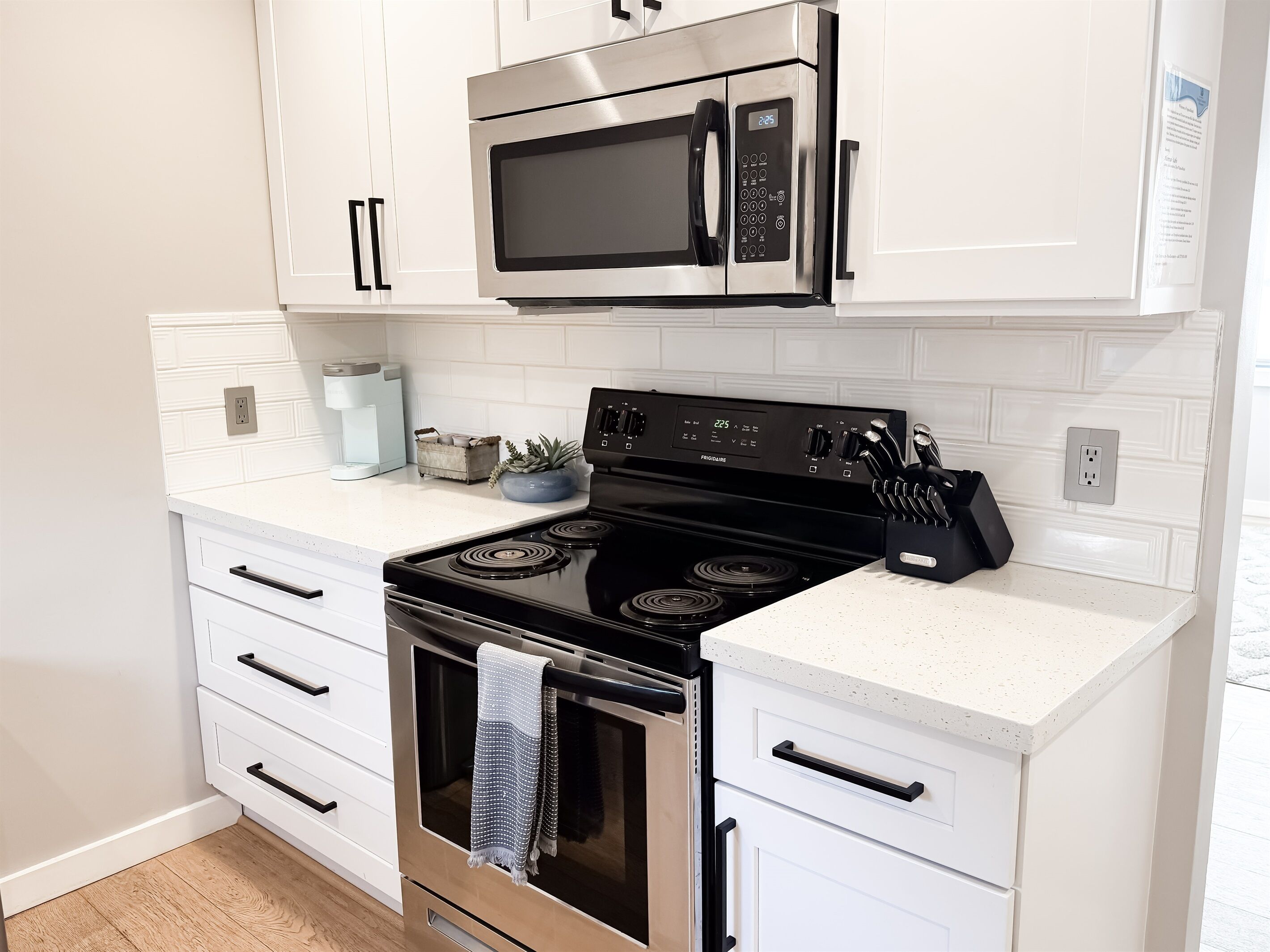 Una cocina moderna con armarios blancos, estufa de acero inoxidable, microondas y cafetera.