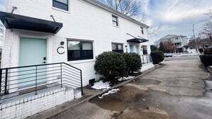 Un immeuble résidentiel blanc à deux étages, avec une porte bleu clair, un petit jardin devant et un ciel dégagé.