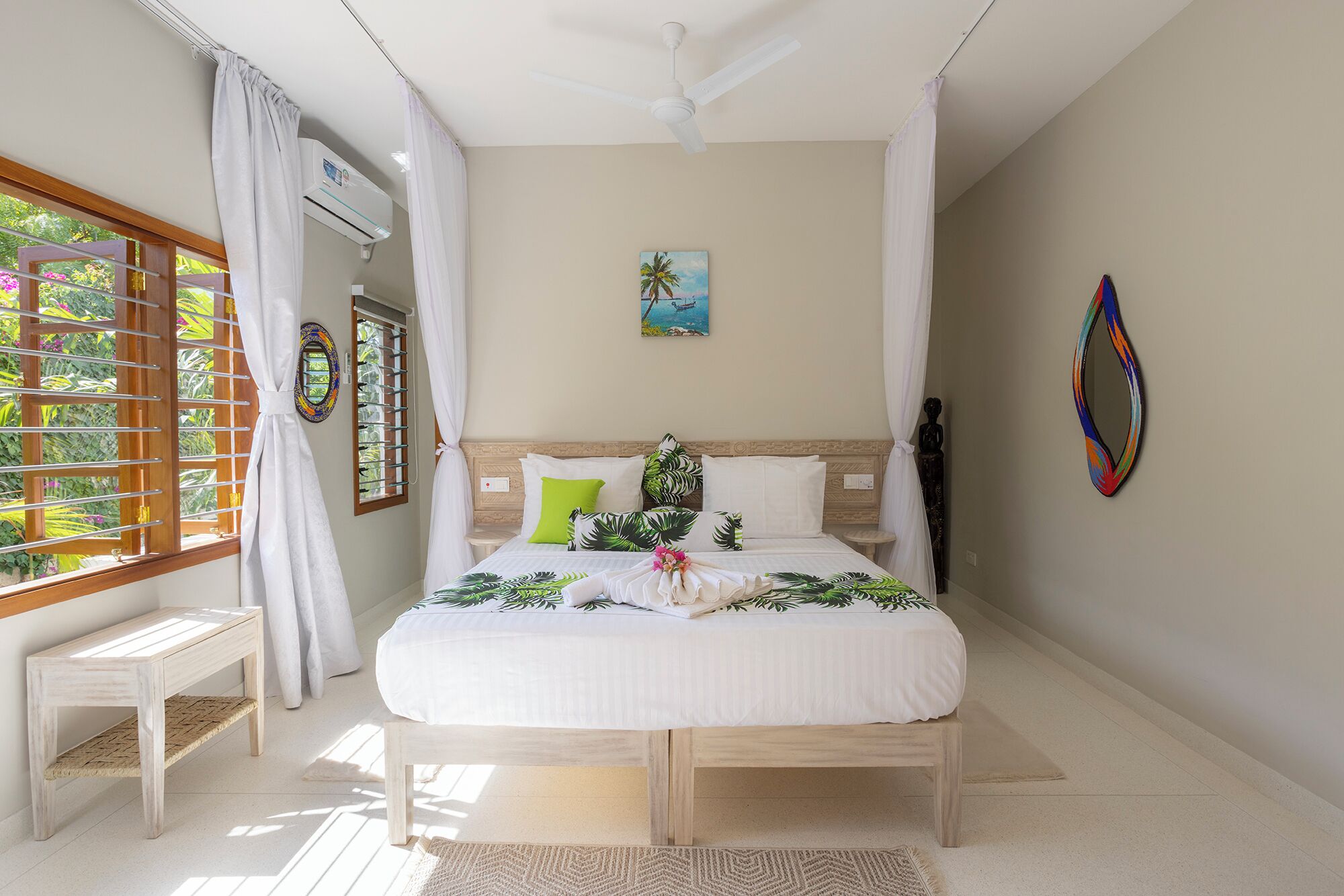 A bedroom with a bed, a ceiling fan, a window with curtains, a bedside table, and a wall with a painting.
