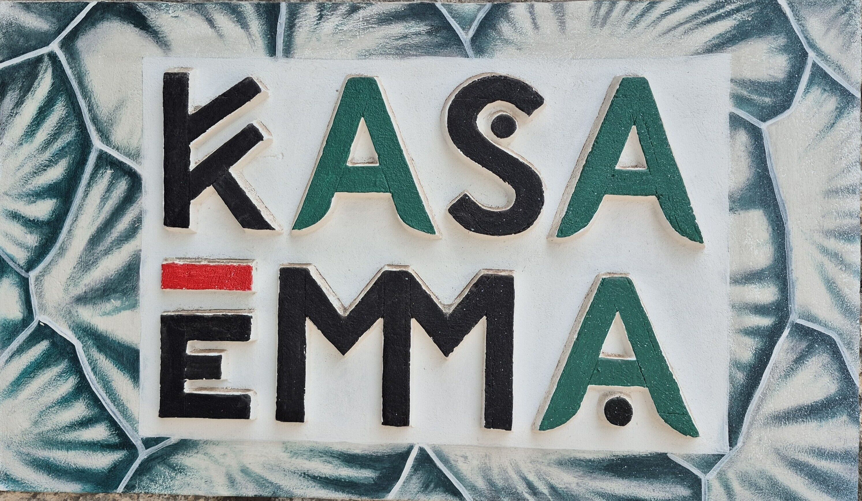 Une enseigne avec le texte « KASA EMMA » en lettres noires et vertes sur un fond blanc.