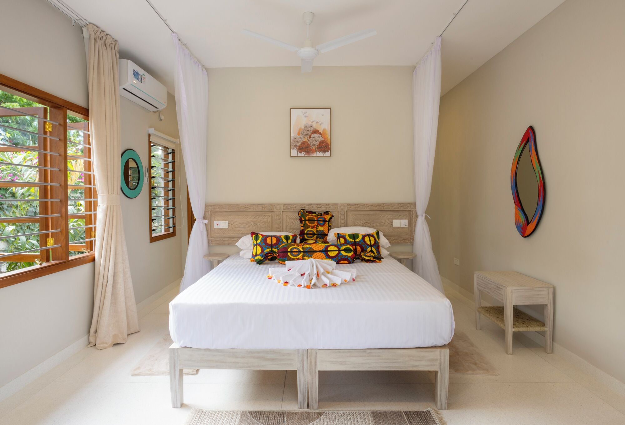 A bedroom with a bed, a ceiling fan, a window with curtains, a bedside table, and a wall-mounted air conditioner.
