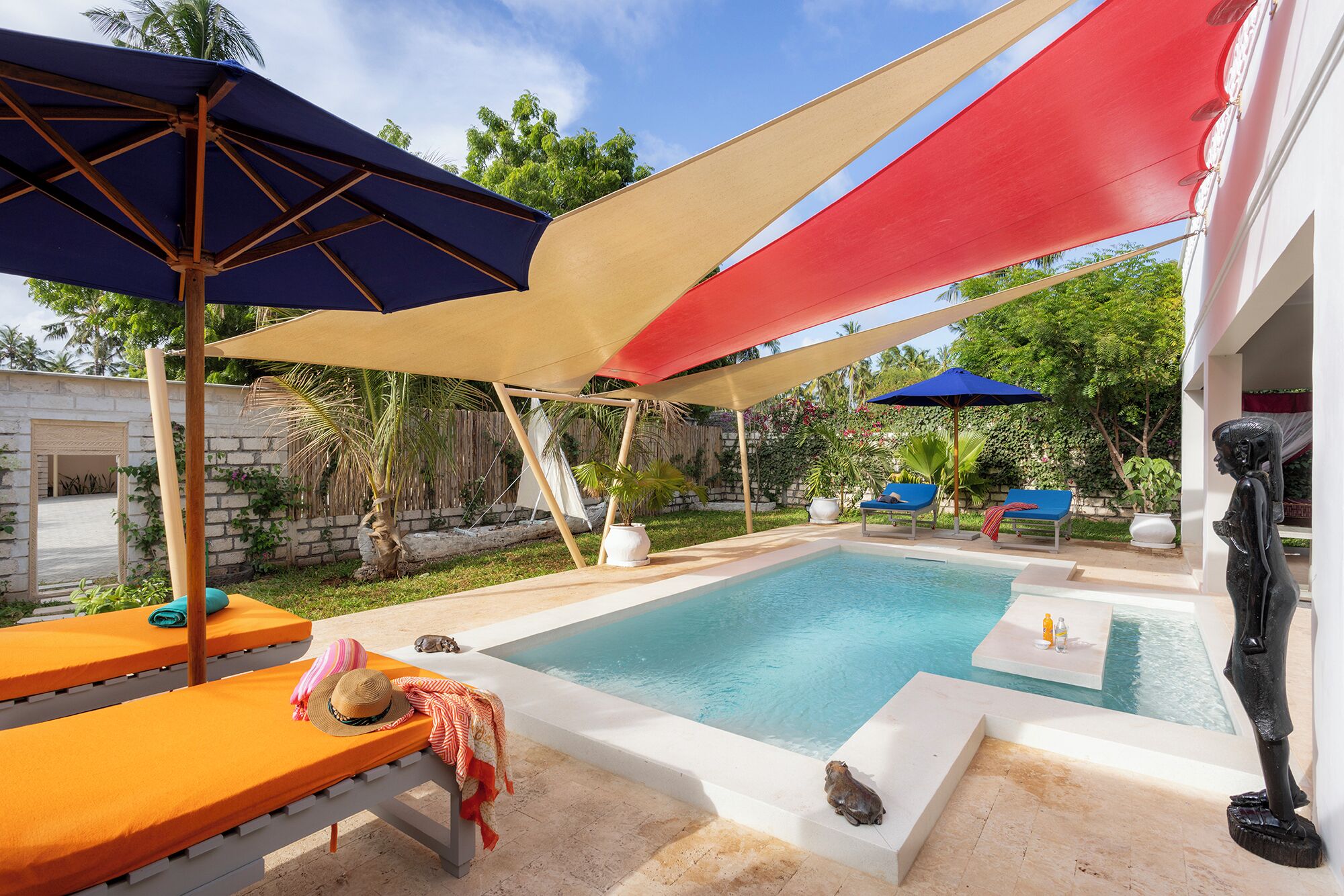 A swimming pool with sun loungers and umbrellas, surrounded by greenery.