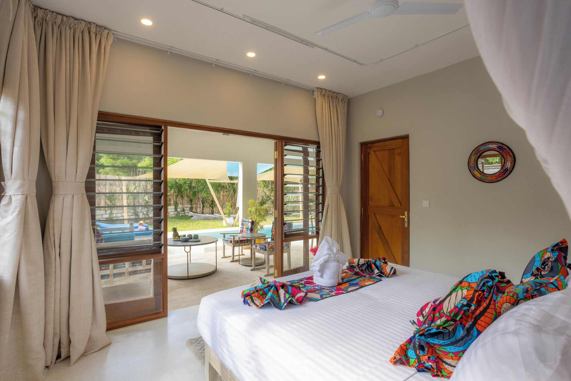 A hotel room with a bed, a small table, and a view of a pool and outdoor area.