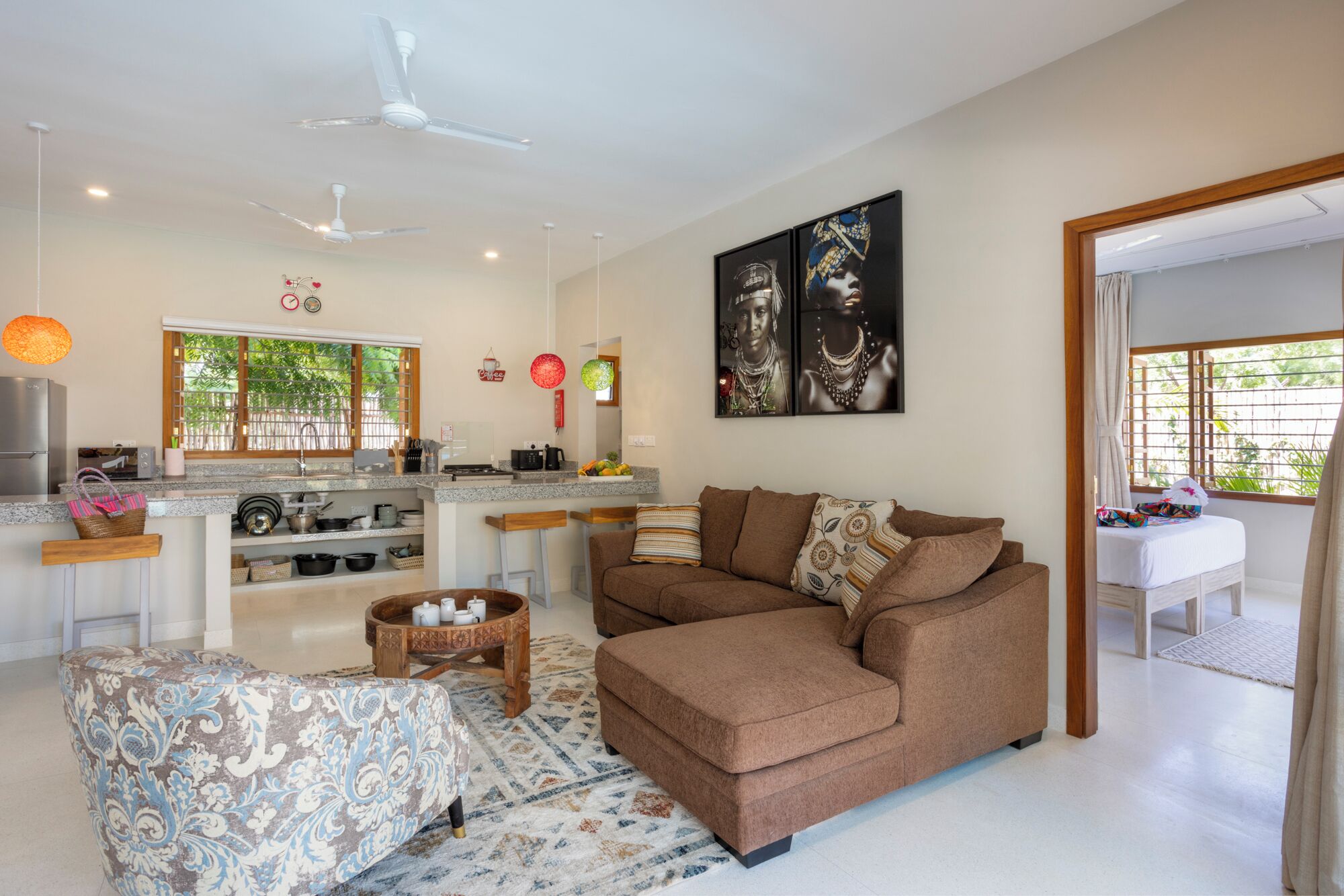 Una sala de estar moderna con un sofá marrón, un otoman con estampado y una zona de cocina con una mesa de comedor.