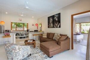 Una sala de estar moderna con un sofá marrón, un otoman con estampado y una zona de cocina con una mesa de comedor.