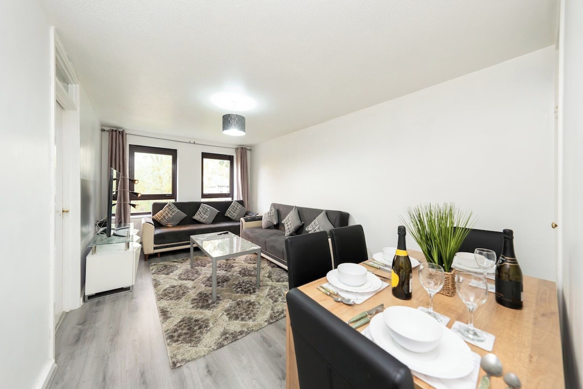 Un salon moderne avec un canapé, une table à manger dressée pour deux personnes et un coin cuisine en arrière-plan.
