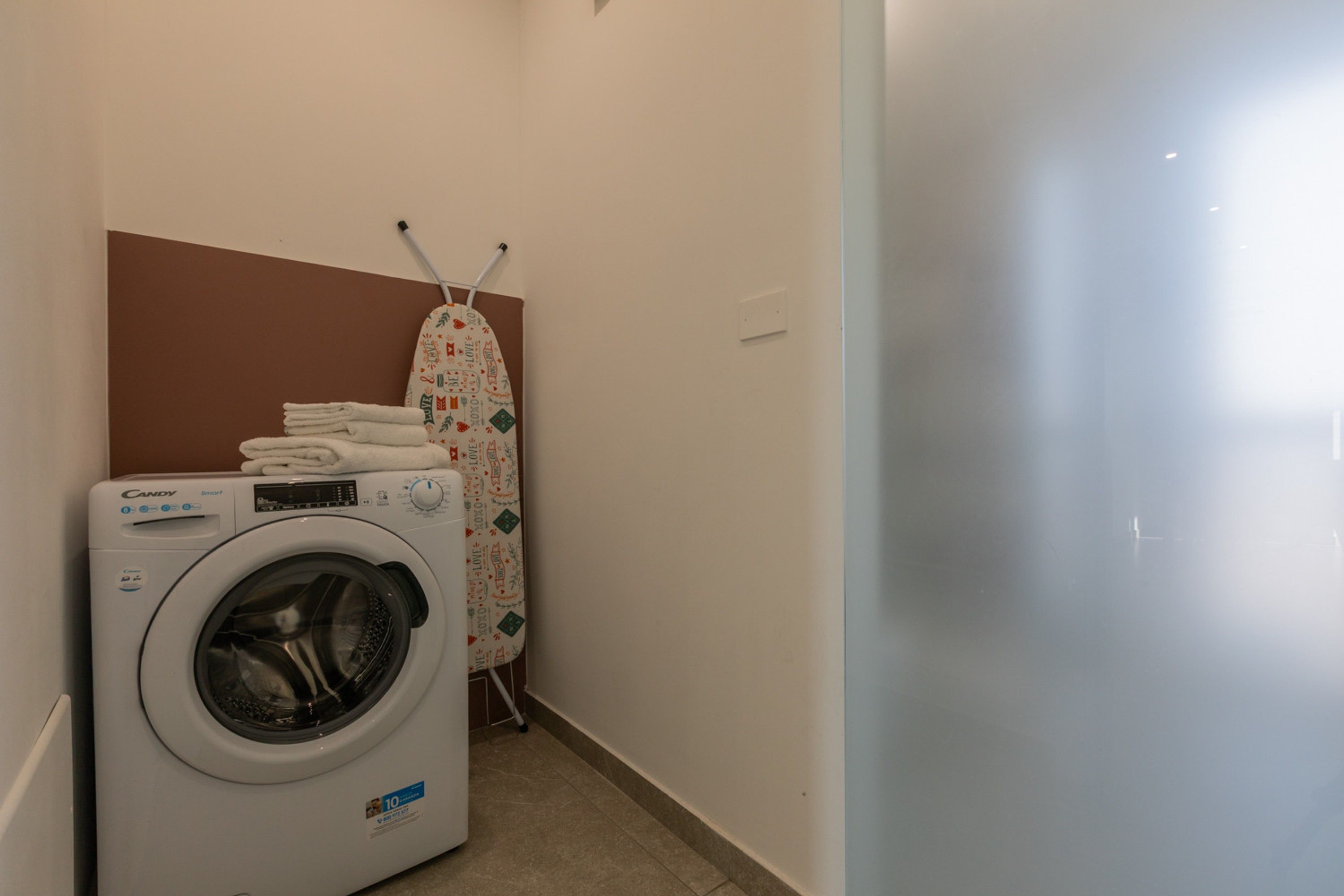 A compact laundry area with a Candy brand washing machine, a drying rack, and neatly folded towels.
