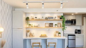 A modern kitchen with white cabinetry, a central island with stools, a microwave, and a refrigerator. - Urban Chic Meets Island Serenity in Waikiki (Honolulu)
