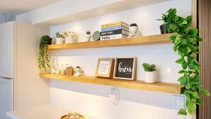 A kitchen with three wooden shelves, each holding books, plants, and decorative items. - Urban Chic Meets Island Serenity in Waikiki (Honolulu)