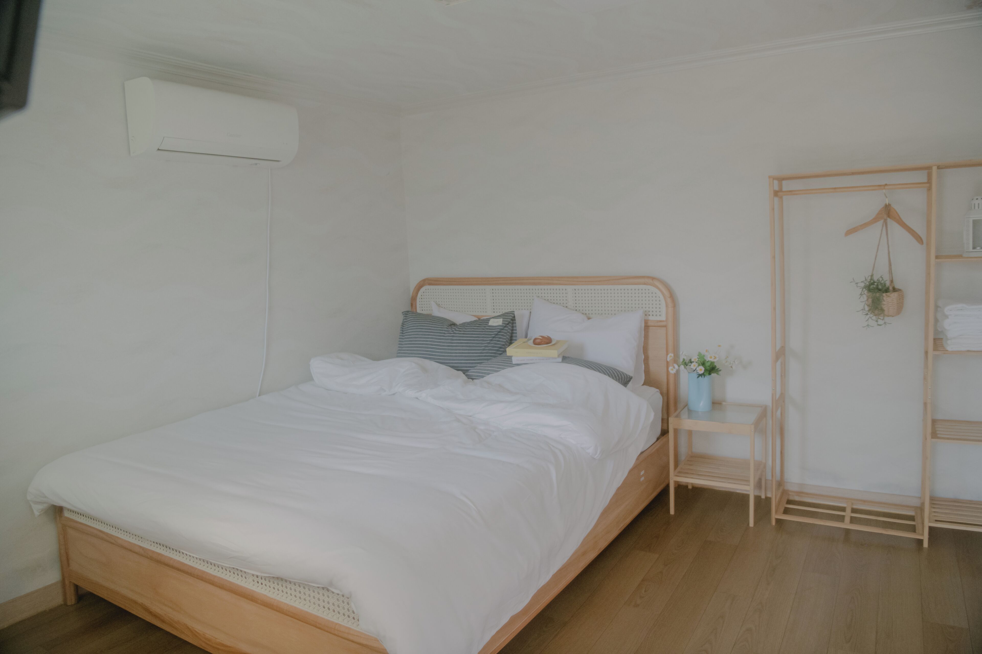 A neatly made bed with white linens, a bedside table with a small plant, and a wooden wardrobe with shelves.