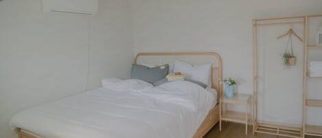 A neatly made bed with white linens, a bedside table with a small plant, and a wooden wardrobe with shelves.