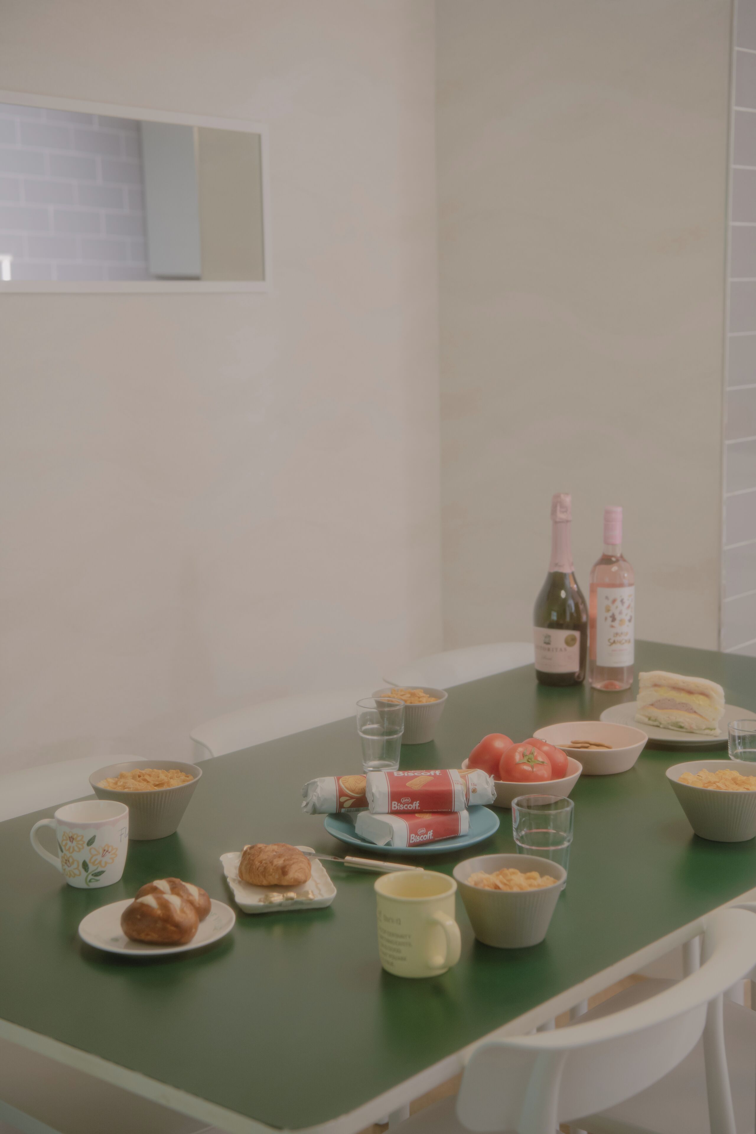 Een eettafel met verschillende soorten eten en drinken, waaronder een fles wijn en een belegd broodje.