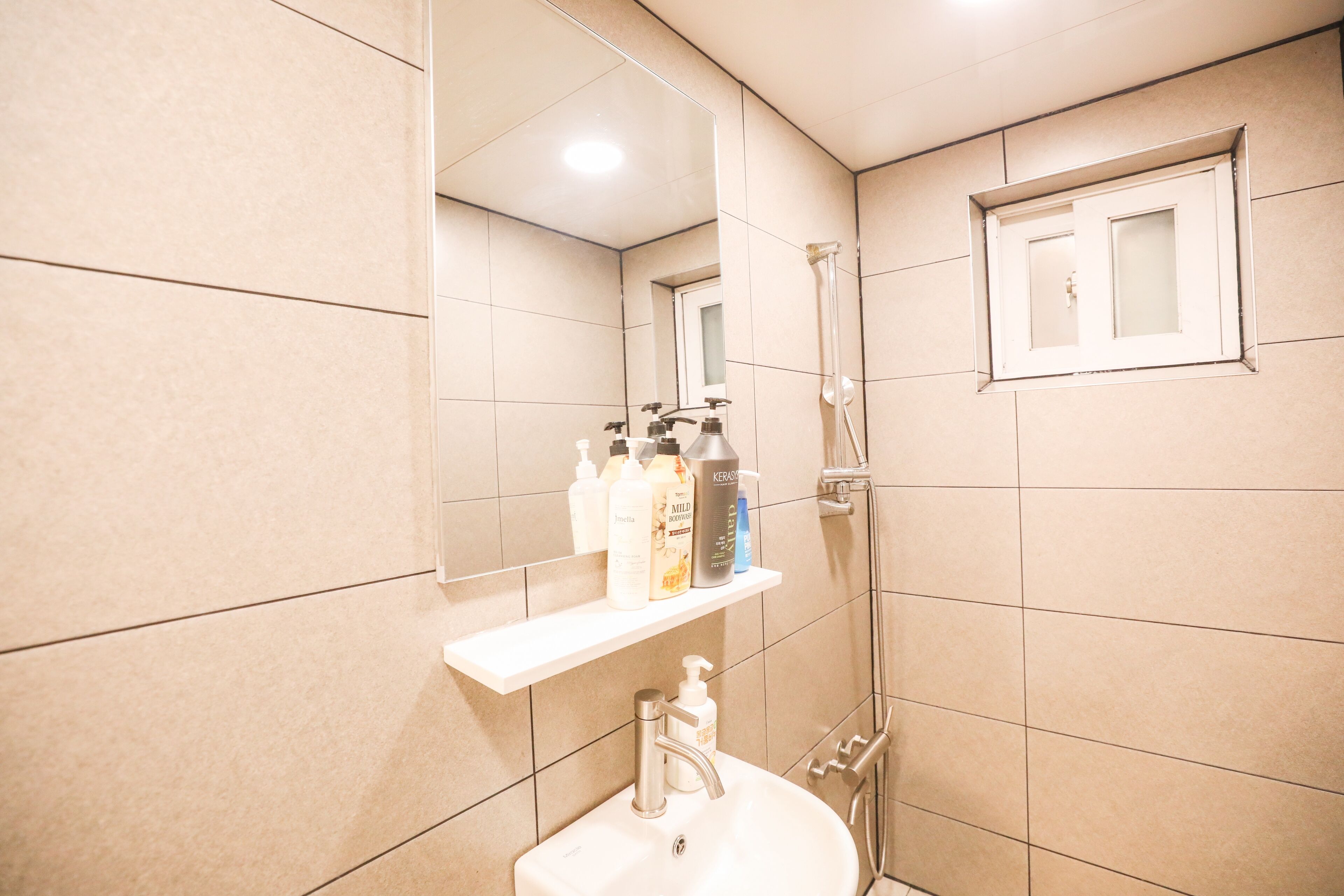 Ein Badezimmer mit Waschbecken, Spiegel und Dusche. Über dem Waschbecken befindet sich ein Ablagefach mit Toilettenartikeln.