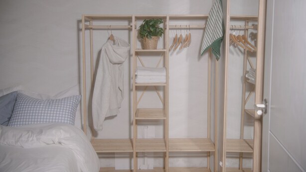 A bedroom with a bed, a wooden wardrobe with shelves, a hanging rack, and a potted plant. - Wave House (Seoul)