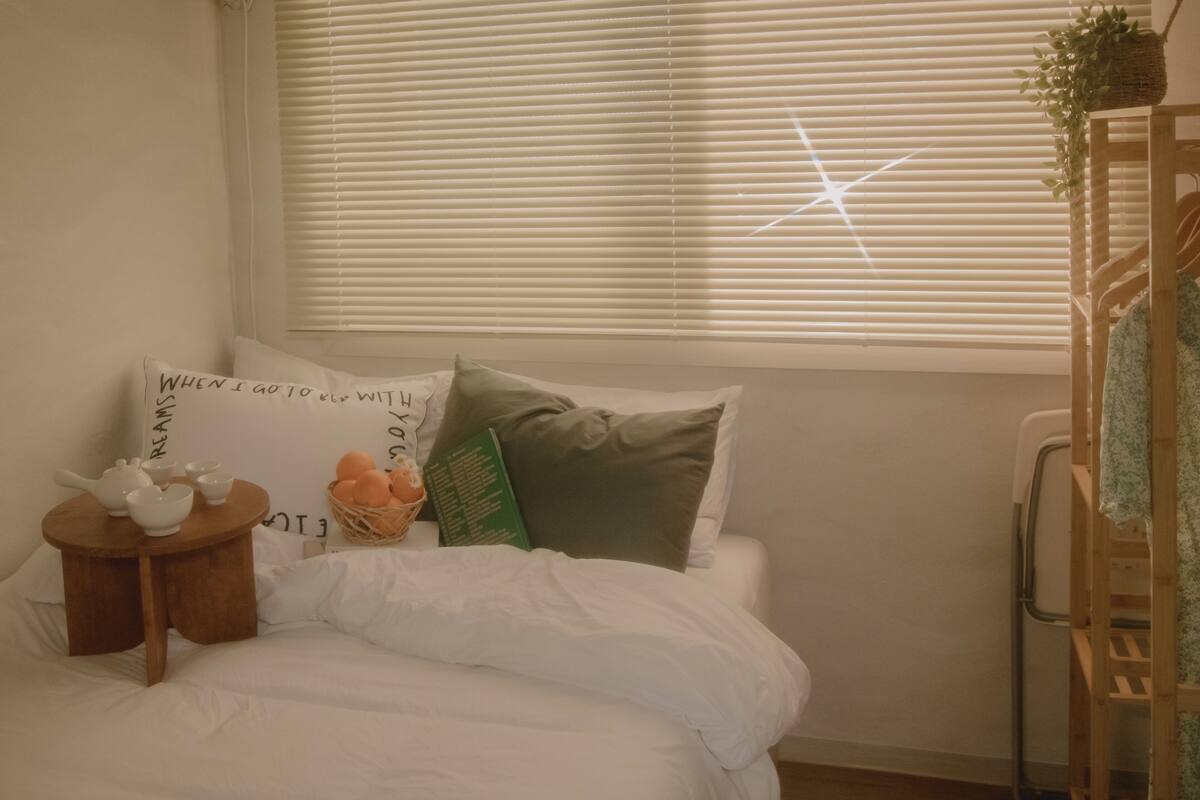 Una camera da letto con un letto, cuscini, un tavolino con teiera, un cesto di uova e una finestra con persiane.