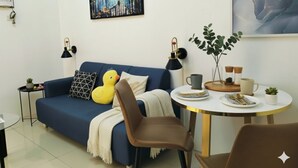 A modern living room with a blue sofa, two black floor lamps, a round dining table with a white tablecloth, and a painting on the wall. - Makati  Business District Residences (Makati)