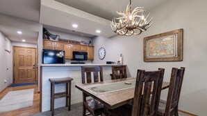 A dining area with a wooden table and chairs, a chandelier, a clock, and a framed map on the wall. - 2BR Village At Indian Point 1107 near SDC - Free Tickets Daily up to $500 (Branson)