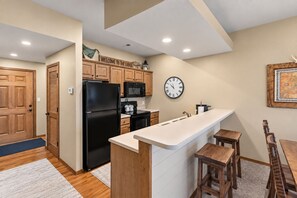Une cuisine moderne avec des meubles en bois, un réfrigérateur noir, un four à micro-ondes et une horloge au mur.