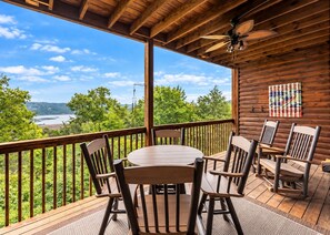 A wooden deck with a round table and chairs, overlooking a body of water and greenery. - 1BR Village At Indian Point 1107 next to SDC- Free Tickets Daily up to $500 (Branson)