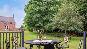 A round outdoor table with four chairs, a bottle of wine, and a glass on the table. - Bewholme (Driffield)