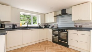 A modern kitchen with white cabinets, a black stove, and a herringbone wood floor. - Bewholme (Driffield)