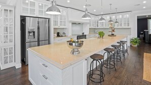 Une cuisine moderne avec des meubles blancs, des appareils en acier inoxydable et un îlot central doté de tabourets de bar.