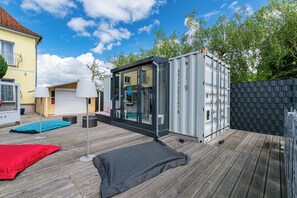 Une terrasse extérieure moderne avec une enceinte en verre, une terrasse en bois et un tapis rouge et noir.