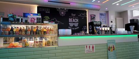 A bar area with a neon sign reading "Enjoy the Beach" and a menu board for cocktails.