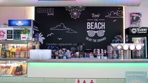 Eine Bar mit einem schwarzen Wandbereich, der den Schriftzug 'The Beach' und verschiedene Flaschen mit Getränken zeigt.