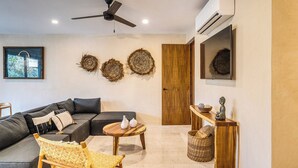A modern living room with a sectional sofa, a wooden coffee table, a wicker chair, and a ceiling fan. - Chic 3-bedroom PENTHOUSE with private Pool & Sunset Terrace - Tulum (Tulum)