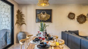 A dining area with a wooden table set for four, surrounded by chairs, a sofa, and a decorative wall piece. - Chic 3-bedroom PENTHOUSE with private Pool & Sunset Terrace - Tulum (Tulum)