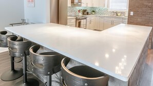 A modern kitchen with a large island, bar stools, pendant lights, and a brick accent wall.