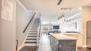 A modern kitchen with a central island, a staircase, and pendant lighting.