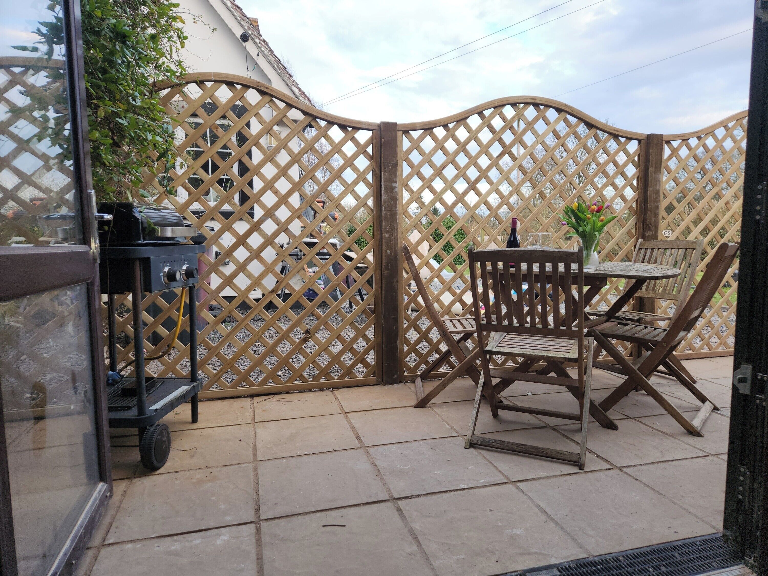 An outdoor patio area with a grill, a table with chairs, and a decorative fence.