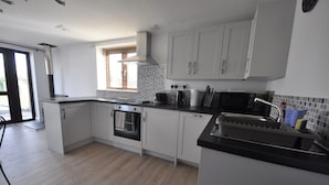 A modern kitchen with white cabinets, a black countertop, a built-in oven, a microwave, and a sink with a dish rack.