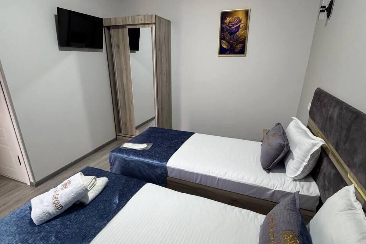 A hotel room with two beds, a TV mounted on the wall, and a painting above the beds.