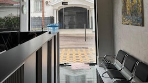 A modern reception area with a glass door leading outside, a reception desk, and a seating area with chairs. - Shams Art Hotel (Tashkent)